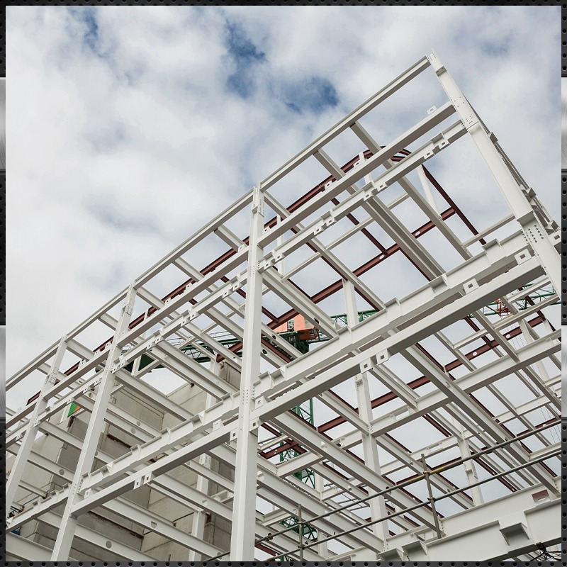 A low-angle view of the white steel framework of a building under construction, set against a cloudy sky with patches of blue.