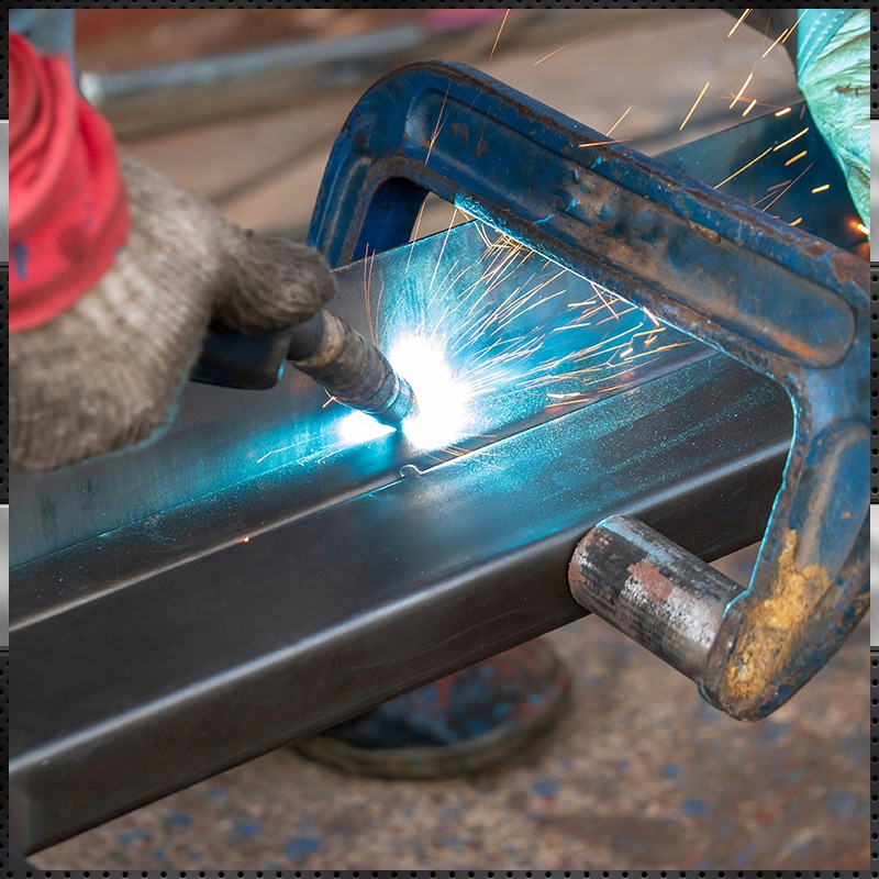 Close-up of a worker welding metal with a clamp securing steel beams in a workshop, producing bright sparks