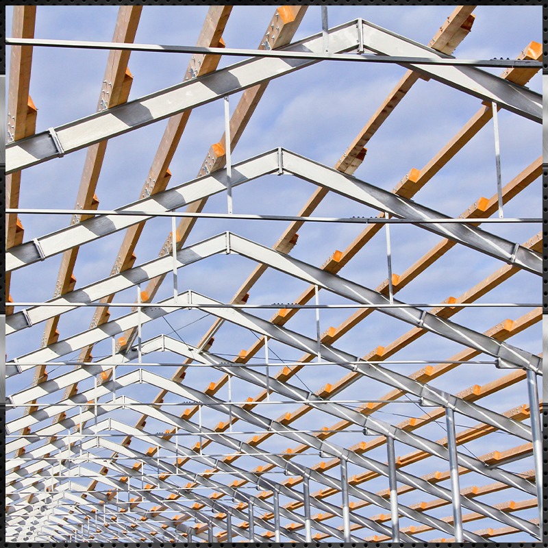The structural framework of a new commercial or agricultural building, showcasing a hybrid system of galvanized steel roof trusses and wooden purlins. This construction method illustrates modern steel frame building techniques.