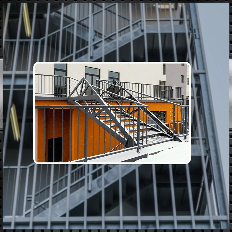 Modern exterior metal stairs featuring grey steel railings and safety grating, set against a vibrant orange building facade.
